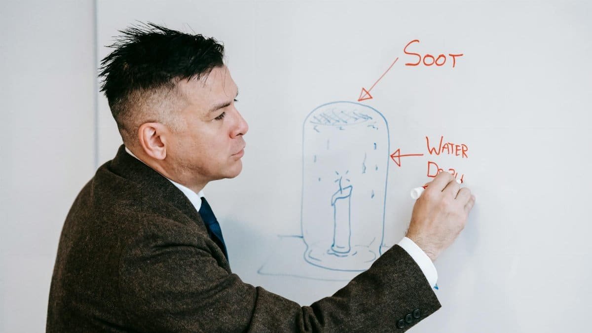 Educator illustrating scientific concepts on whiteboard with marker, explaining soot and water displacement.