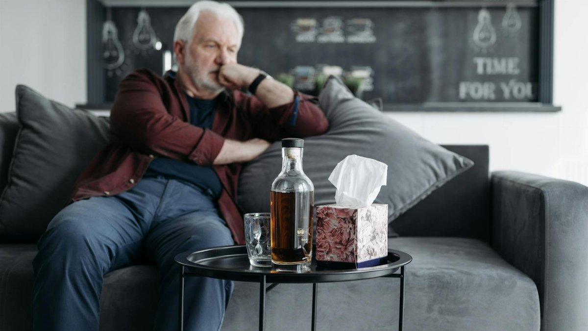 A senior man sits pensively with a bottle of whiskey, evoking a somber mood.