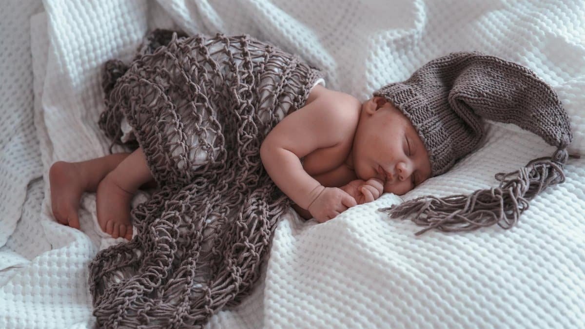 Charming image of a newborn baby napping peacefully, draped in a cozy knit blanket.