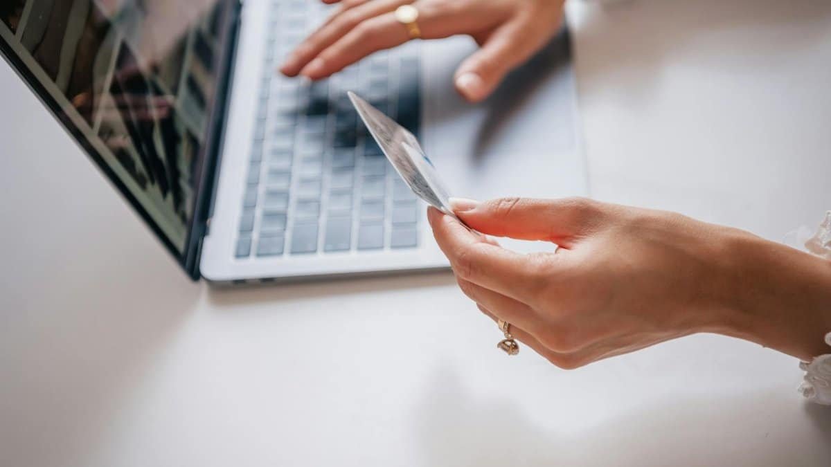 Close-up of woman holding a credit card while typing on a laptop, representing online shopping.
