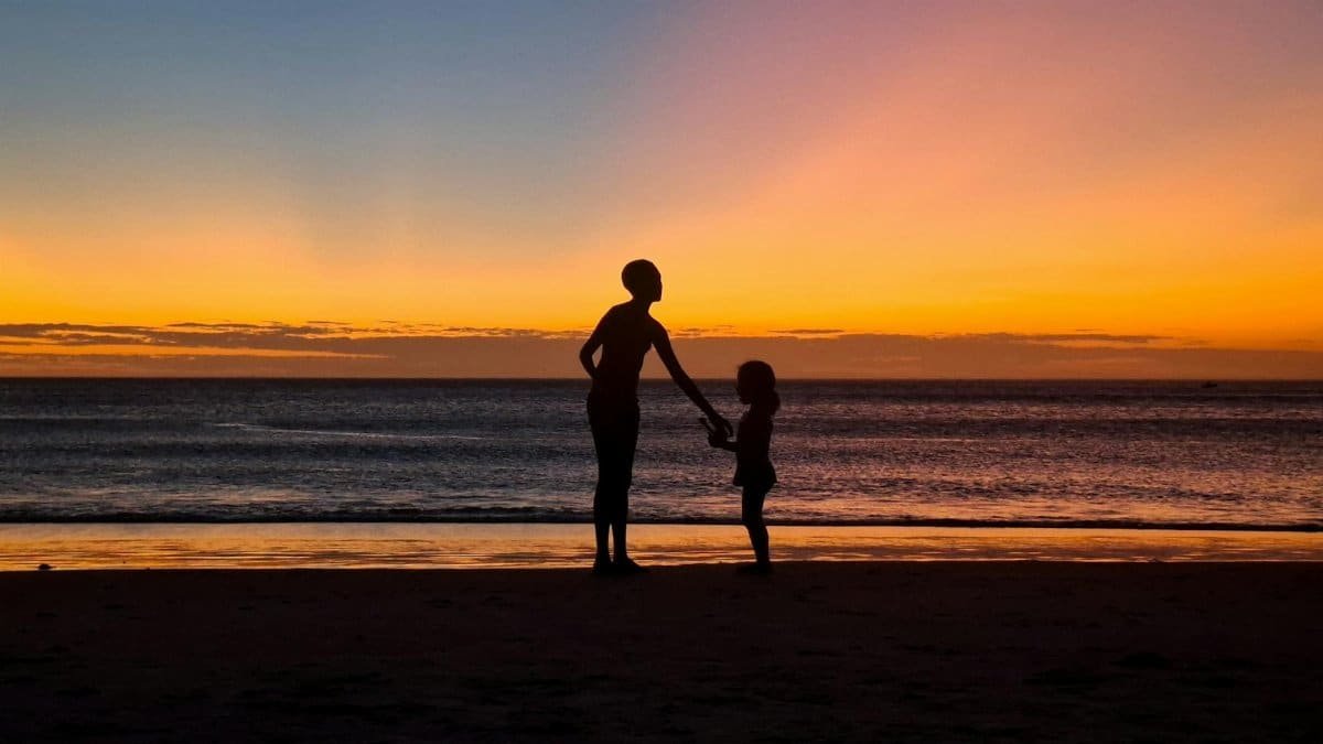 Silhouetted family enjoying a serene sunset on Arraial do Cabo beach, Brazil.