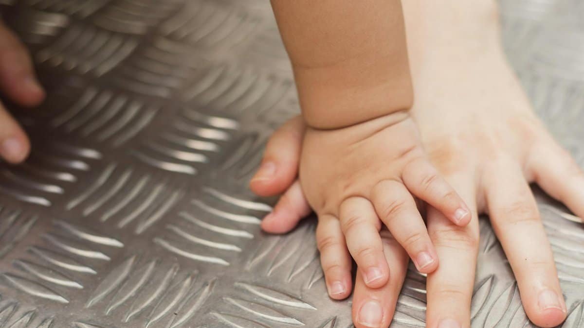 A tender close-up capturing a baby's hand gently touching an adult's hand on a metallic background.