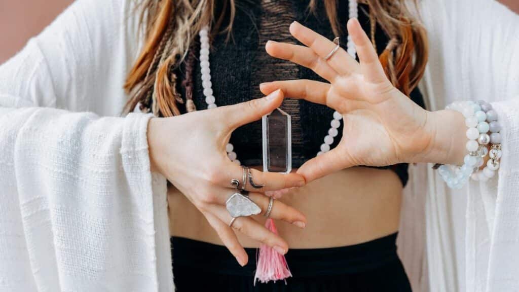 A woman wearing jewelry holds a clear healing crystal, symbolizing spiritual wellness.