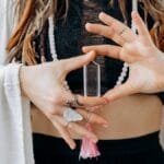 A woman wearing jewelry holds a clear healing crystal, symbolizing spiritual wellness.