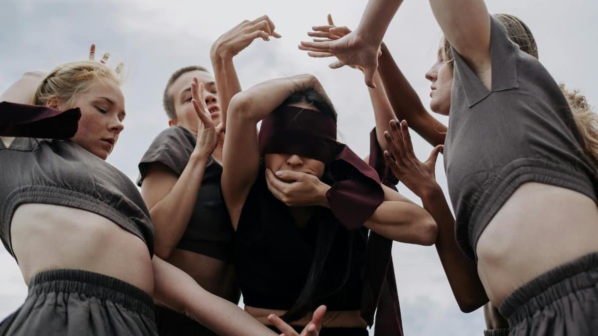 Conceptual dance scene with blindfolded women in gray dresses, creating an eerie and ritualistic atmosphere.