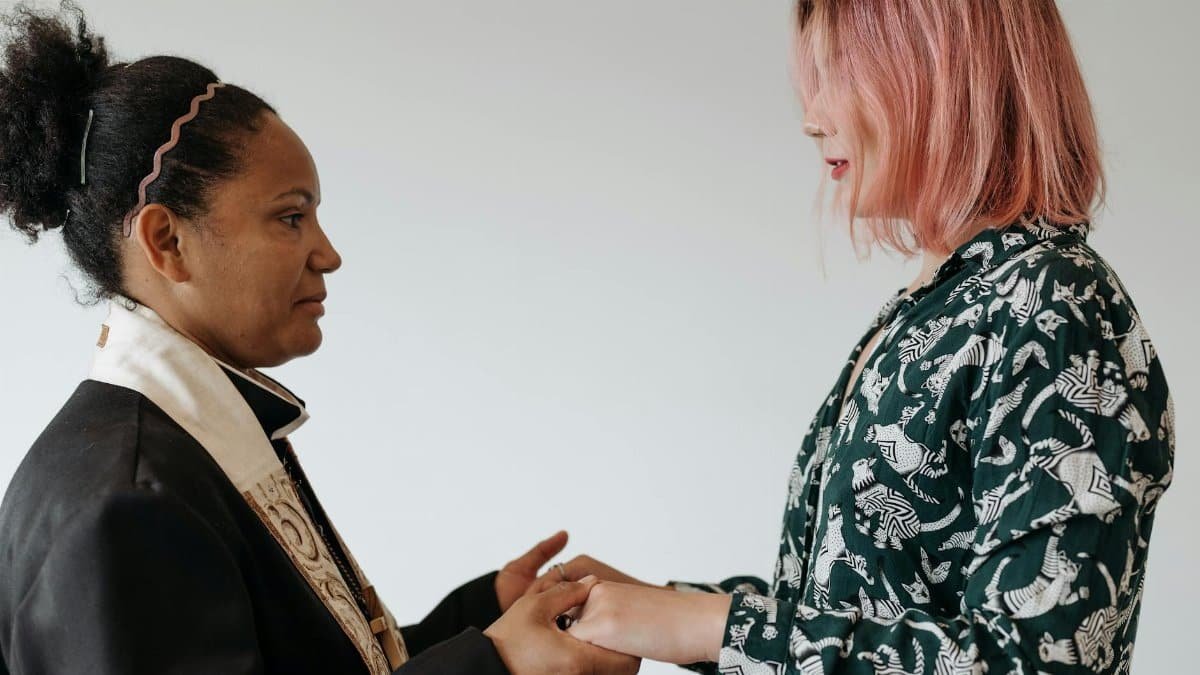 A priest and a woman standing indoors, holding hands in a ritualistic gesture, symbolizing unity and faith.