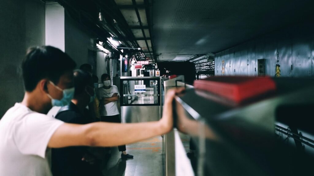 People wearing masks wait on a dimly lit subway platform, conveying urban life.