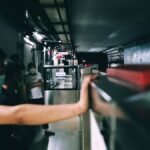 People wearing masks wait on a dimly lit subway platform, conveying urban life.