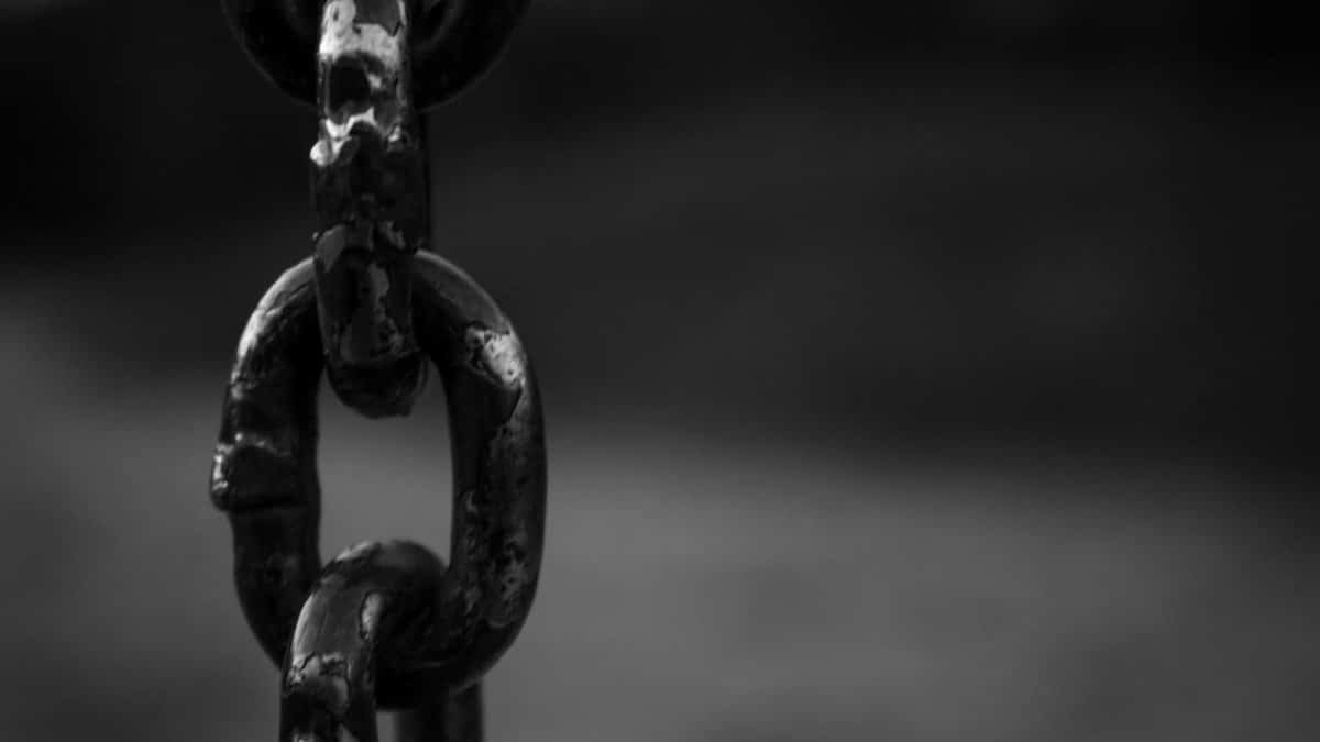 Detailed black and white image of a rusty chain link with blurred background.