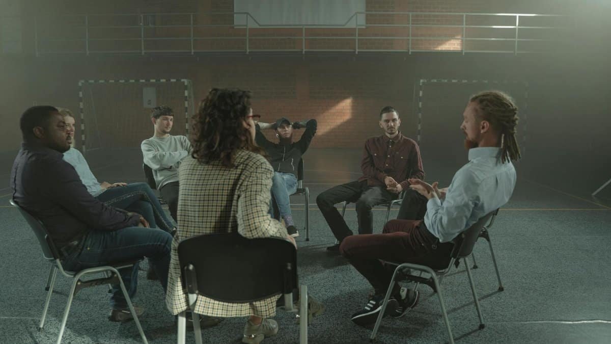 A diverse group engages in a therapy session inside a gym, fostering mental health support.