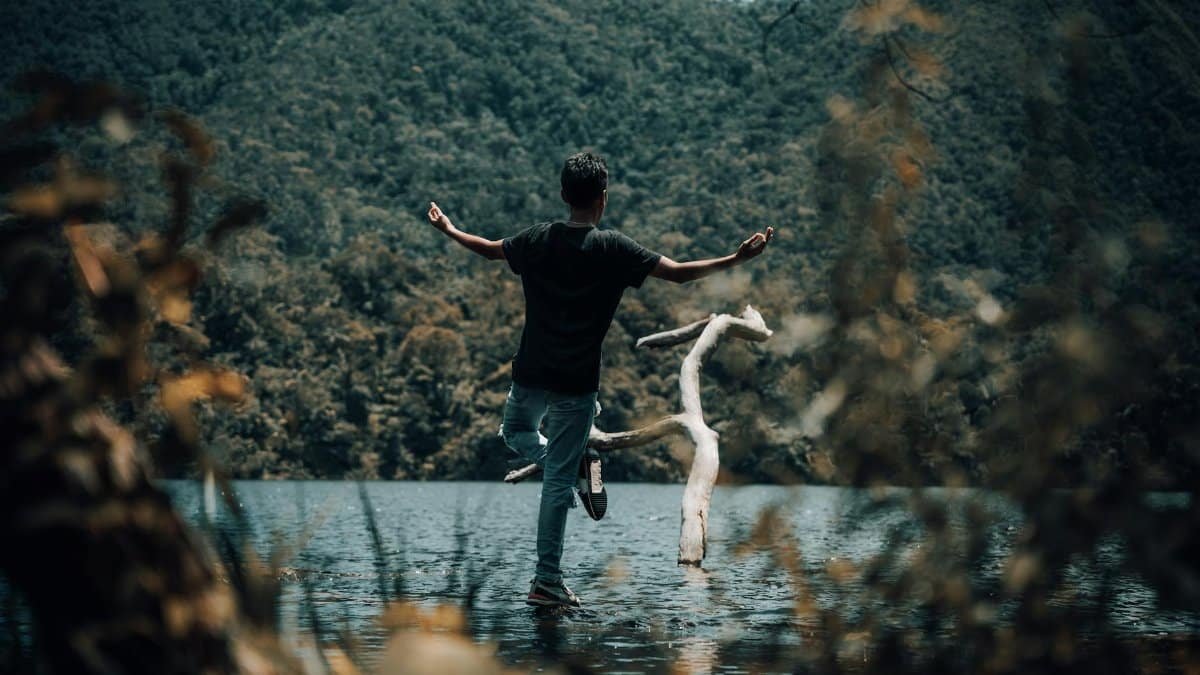 A man practices meditation by a serene lake with lush forest surroundings in San Martín, Perú.