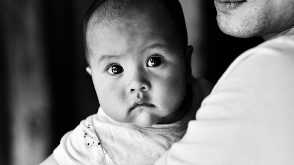 Intimate black and white portrait of a baby being held by a parent, capturing a tender moment.