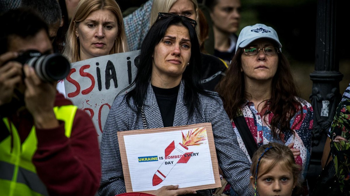 People protesting Ukraine bombings with placards and emotional expressions.
