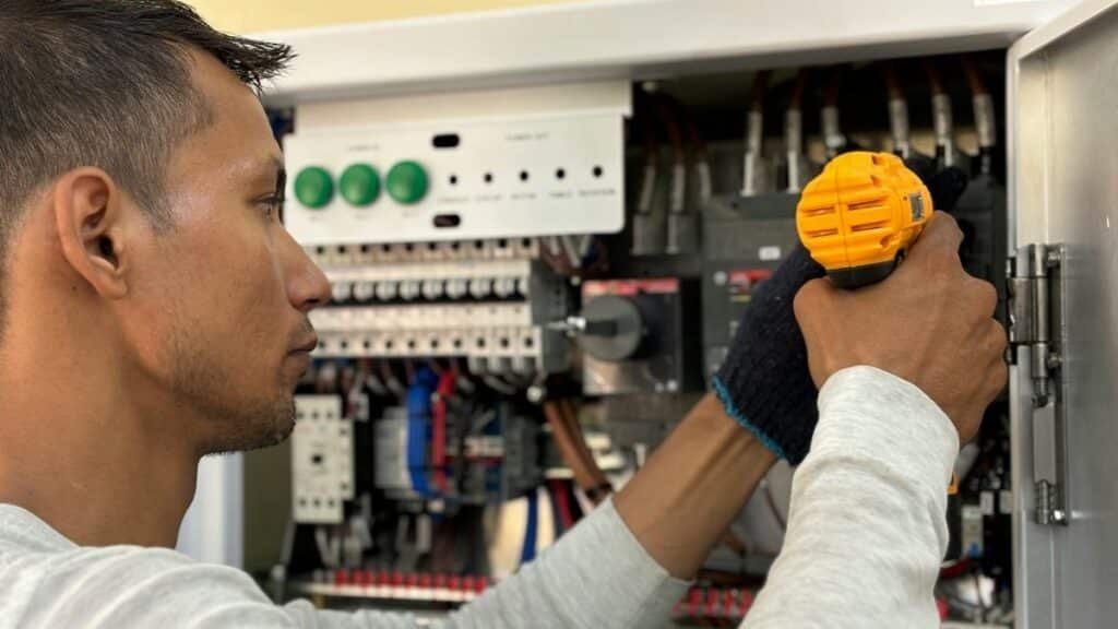 Skilled electrician using a drill to repair electrical equipment indoors. Focus on precision and safety.