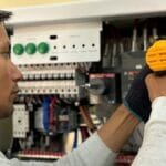 Skilled electrician using a drill to repair electrical equipment indoors. Focus on precision and safety.