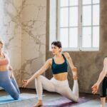 Three women practicing yoga indoors, focusing on flexibility and wellness.