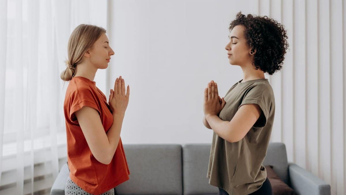 Two women practicing yoga and mindfulness indoors, focusing on relaxation and wellbeing.