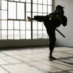 Martial artist in silhouette practicing a high kick in an industrial studio space.