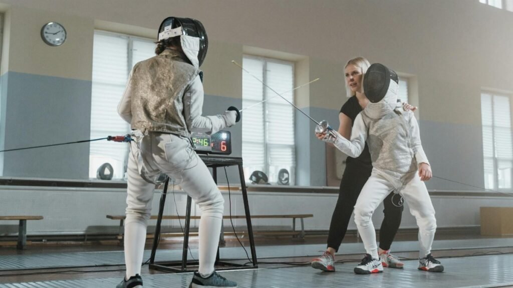 Two fencers practicing under the guidance of a coach in a sports hall.