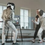 Two fencers practicing under the guidance of a coach in a sports hall.