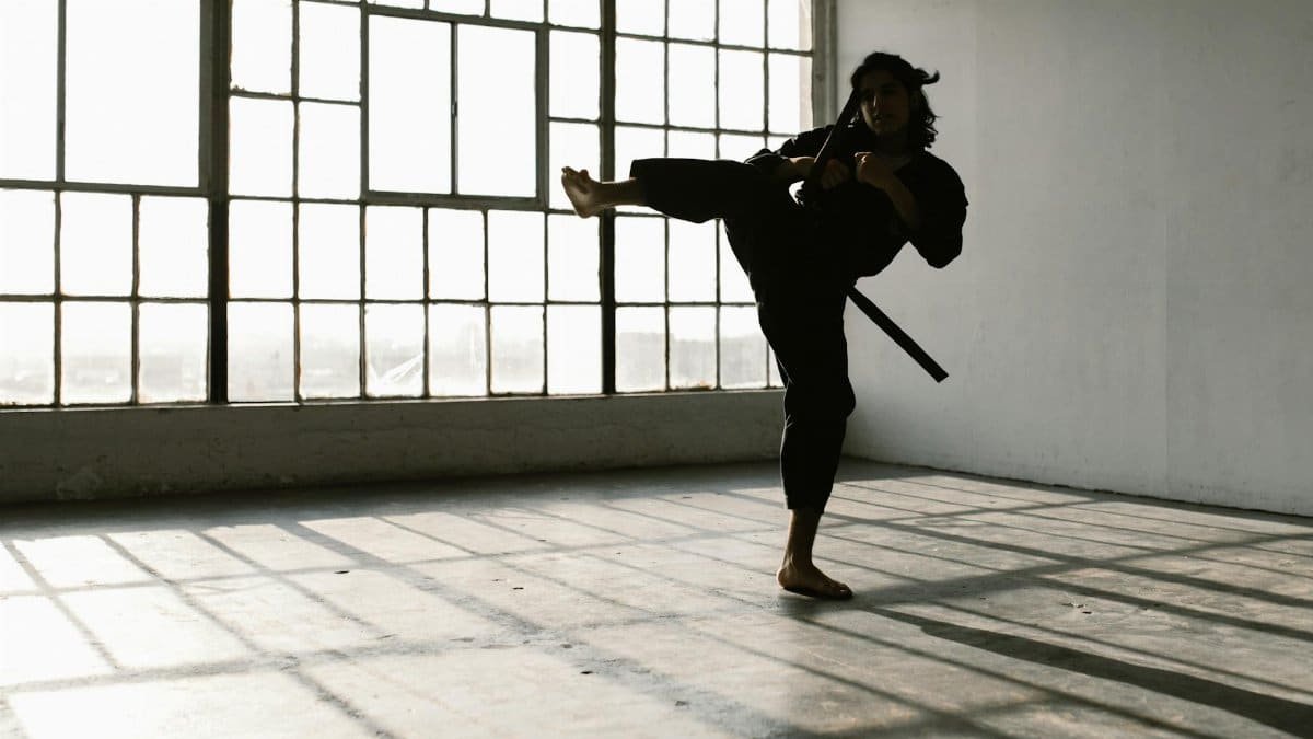 Martial artist in silhouette practicing a high kick in an industrial studio space.