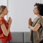 Two women practicing yoga and mindfulness indoors, focusing on relaxation and wellbeing.