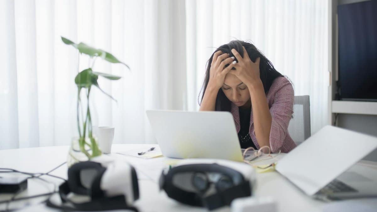 Frustrated woman sitting at desk with laptop, showing stress in a modern office environment.