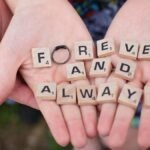 Hands holding 'forever and always' in Scrabble letters, symbolizing eternal love.