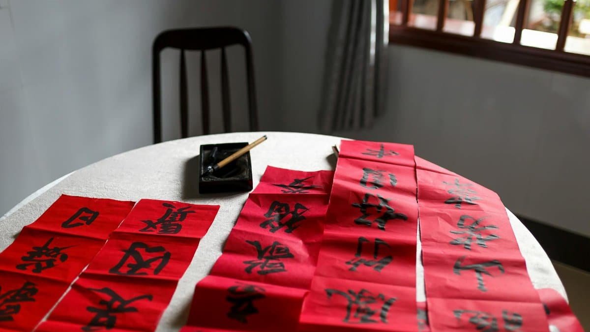 Chinese calligraphy practice with elegant characters on red paper in a serene indoor setting.