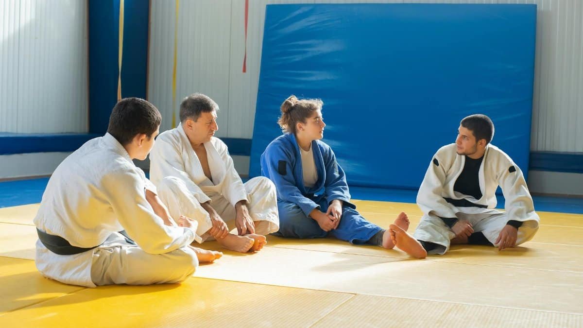 Group of judo practitioners sitting on a mat in a dojo, discussing techniques during training.
