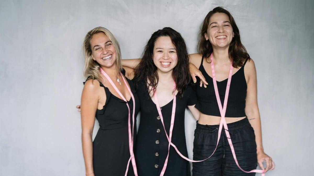 Three women support breast cancer awareness with pink ribbons and smiles.