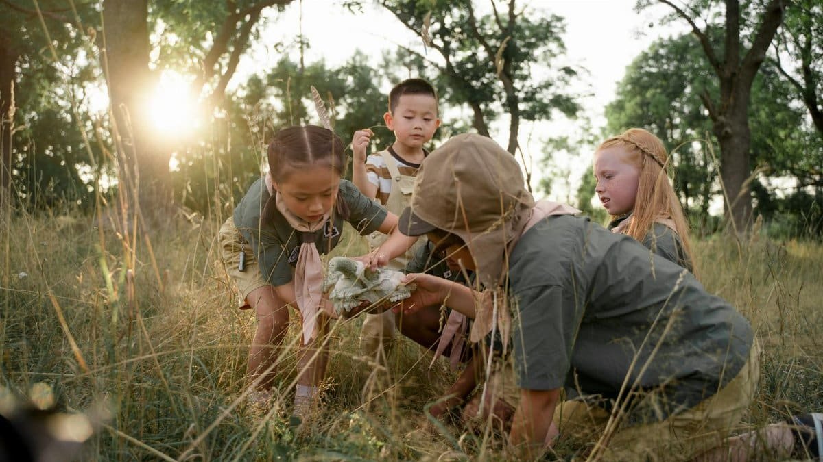 Curious children discover an animal skull in a sunlit forest during summer camp.