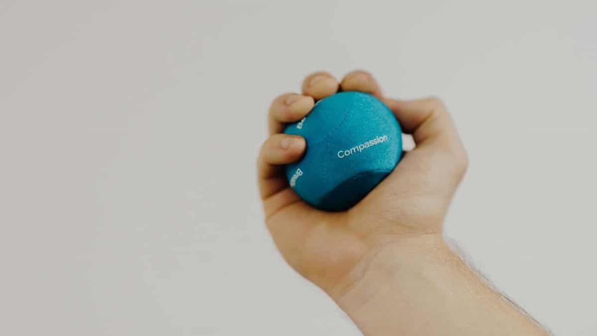 Crop unrecognizable male athlete with small rubber ball in hand exercising during recovery process on light background