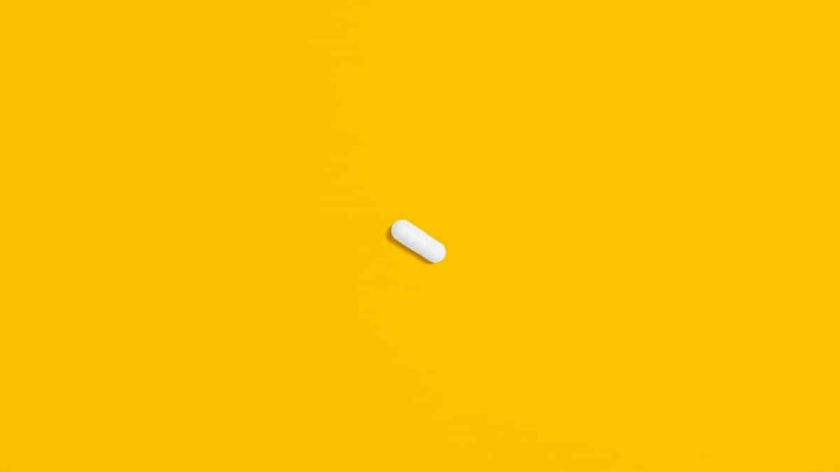 A single white pill lies against a bright yellow background, highlighting its simplicity and focus.