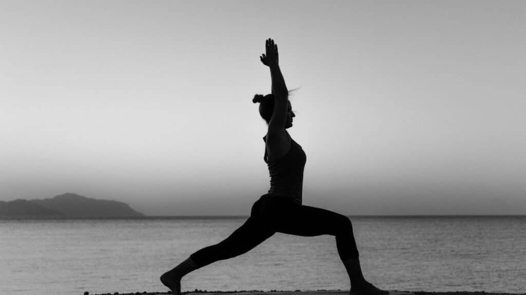 Grayscale silhouette of a woman practicing yoga on a beach at sunset.