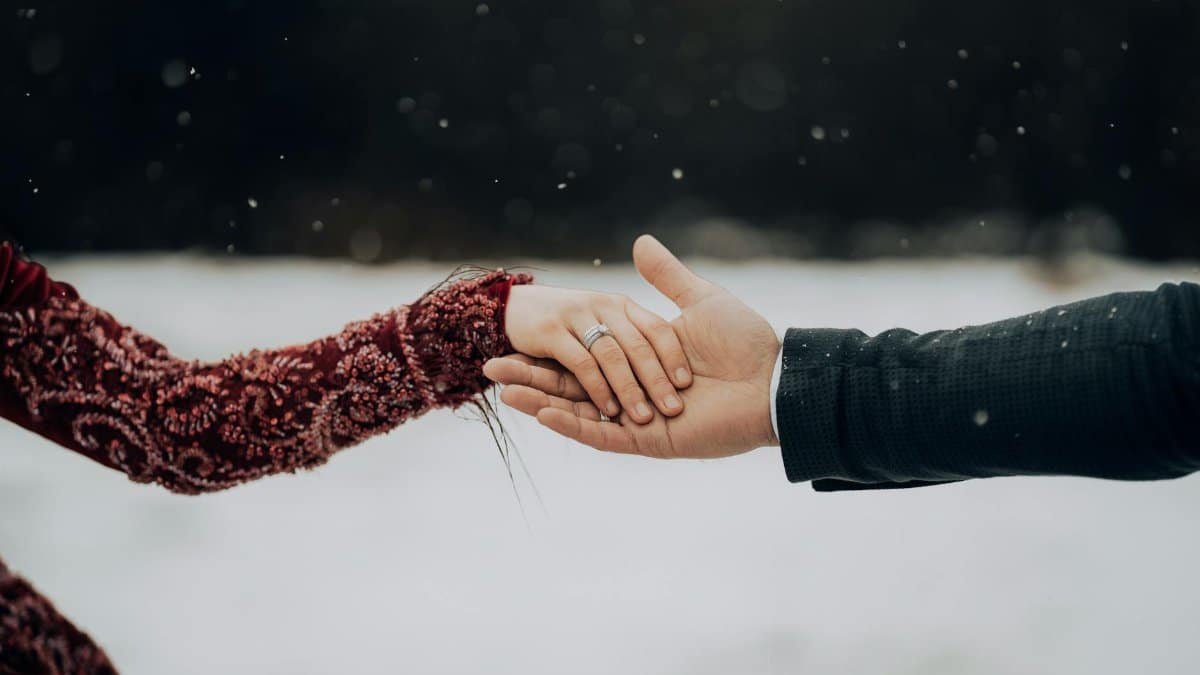 Close-up of a couple holding hands in a snowy setting, embracing love and togetherness.