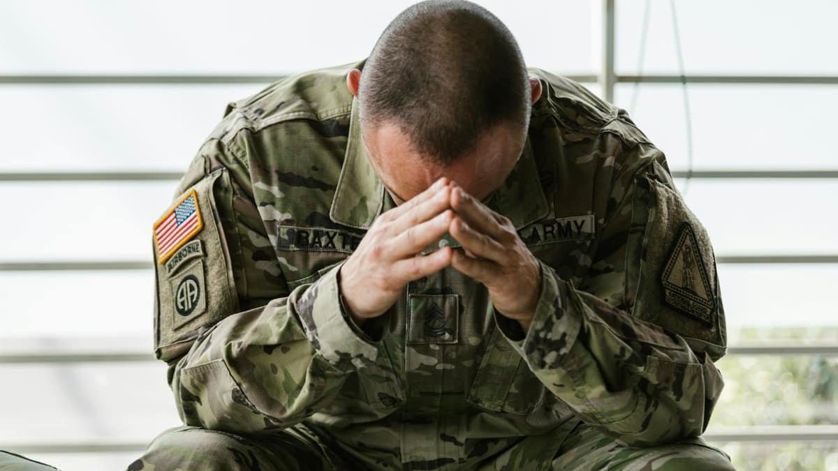 A soldier in camouflage sitting indoors, appearing stressed and overwhelmed.