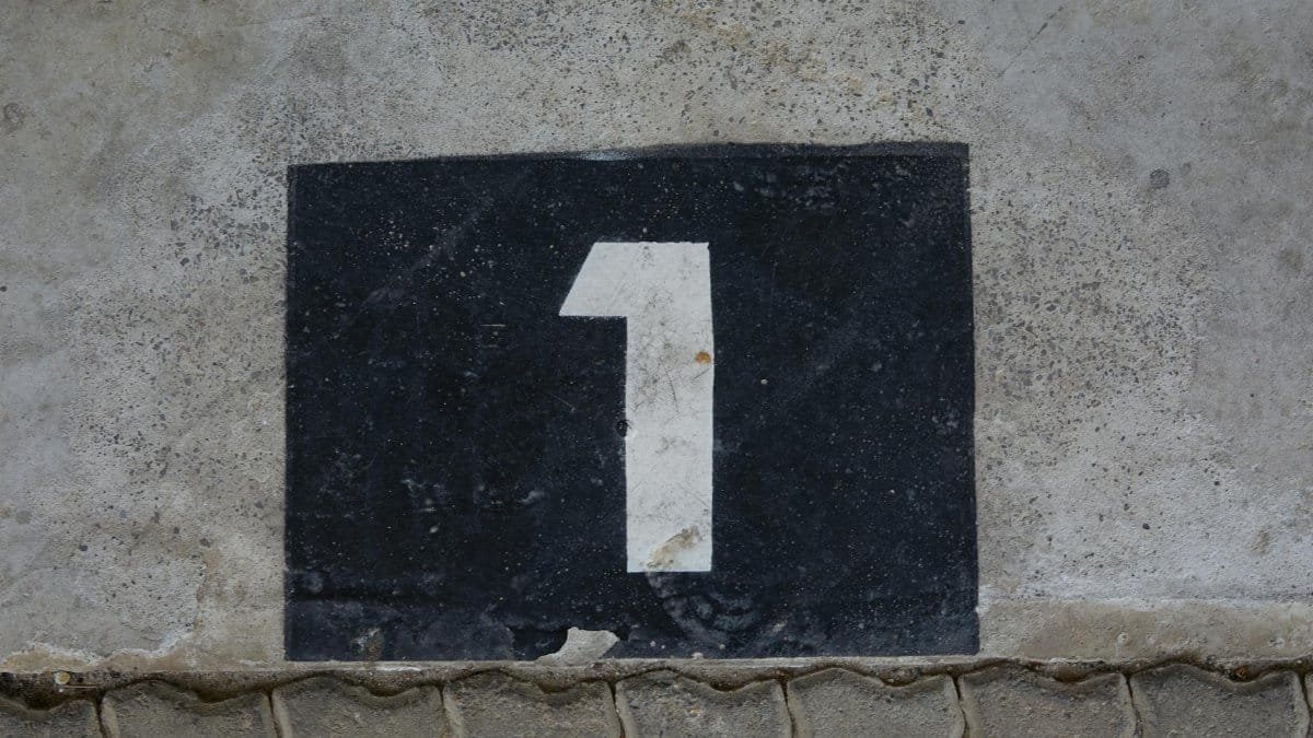 A weathered concrete wall with a bold number one painted on a black rectangular background.
