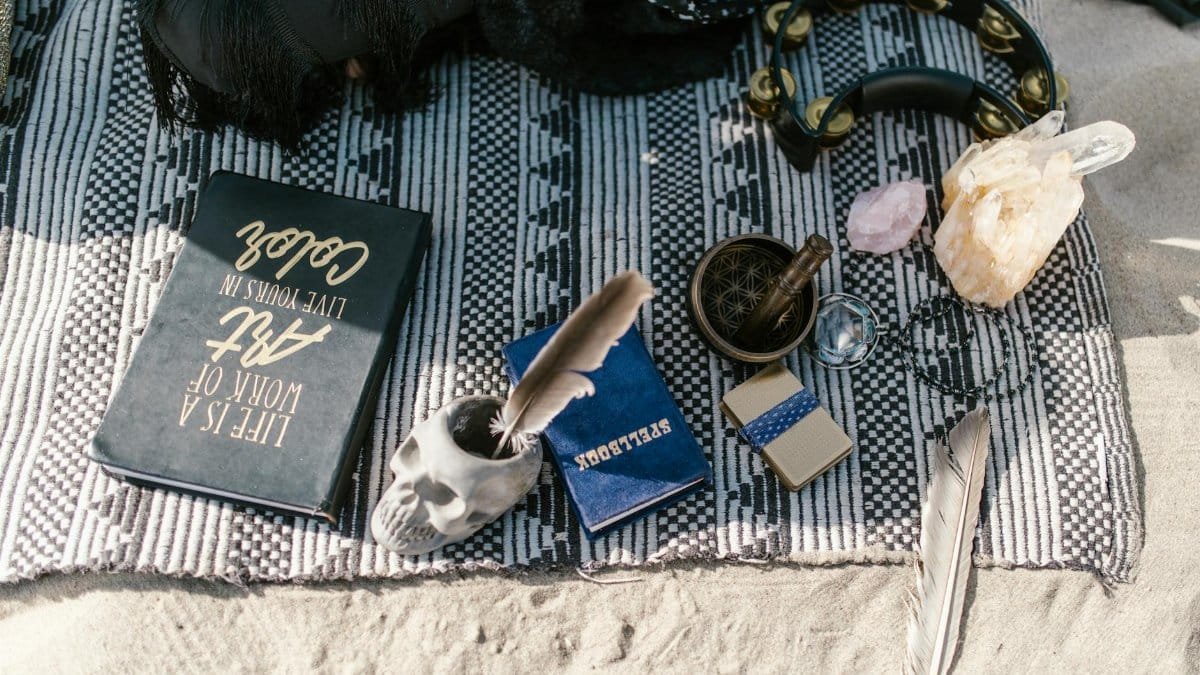 Flat lay of spiritual tools with crystals, skull cup, and feathers on a blanket outdoors.