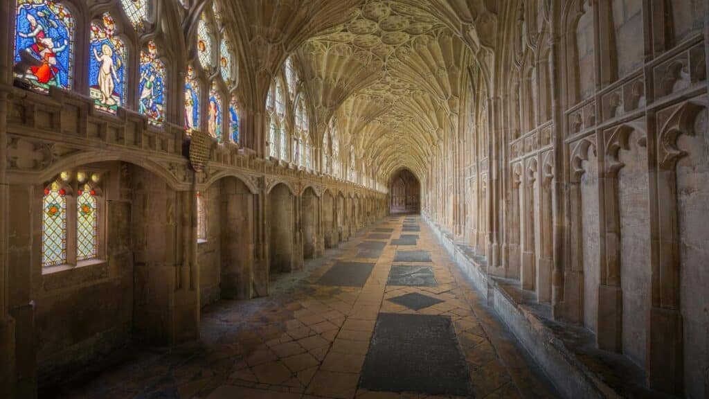 Gothic cloisters of Gloucester Cathedral showcasing intricate arches and vibrant stained glass windows.
