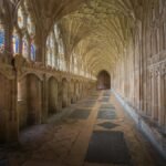 Gothic cloisters of Gloucester Cathedral showcasing intricate arches and vibrant stained glass windows.