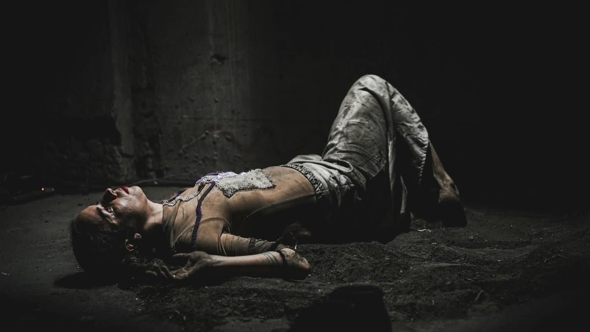 A woman lies on a dark floor, evoking themes of despair and pain.