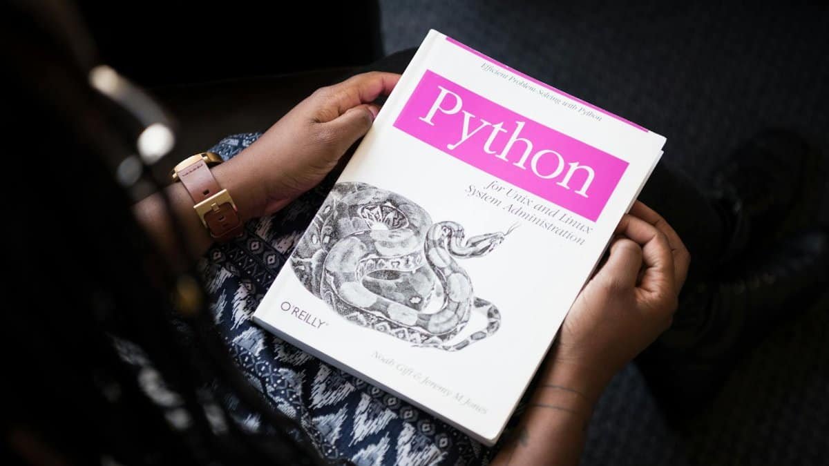 A person reads 'Python for Unix and Linux System Administration' indoors.