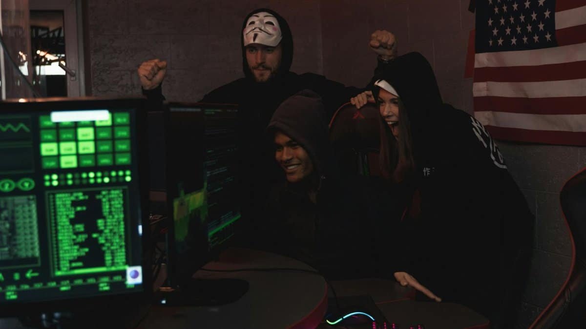 Group of tech enthusiasts in hoodies celebrate a successful cybersecurity operation indoors.