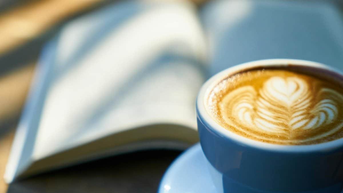 Warm latte art in a blue cup beside an open book, capturing a cozy morning vibe.
