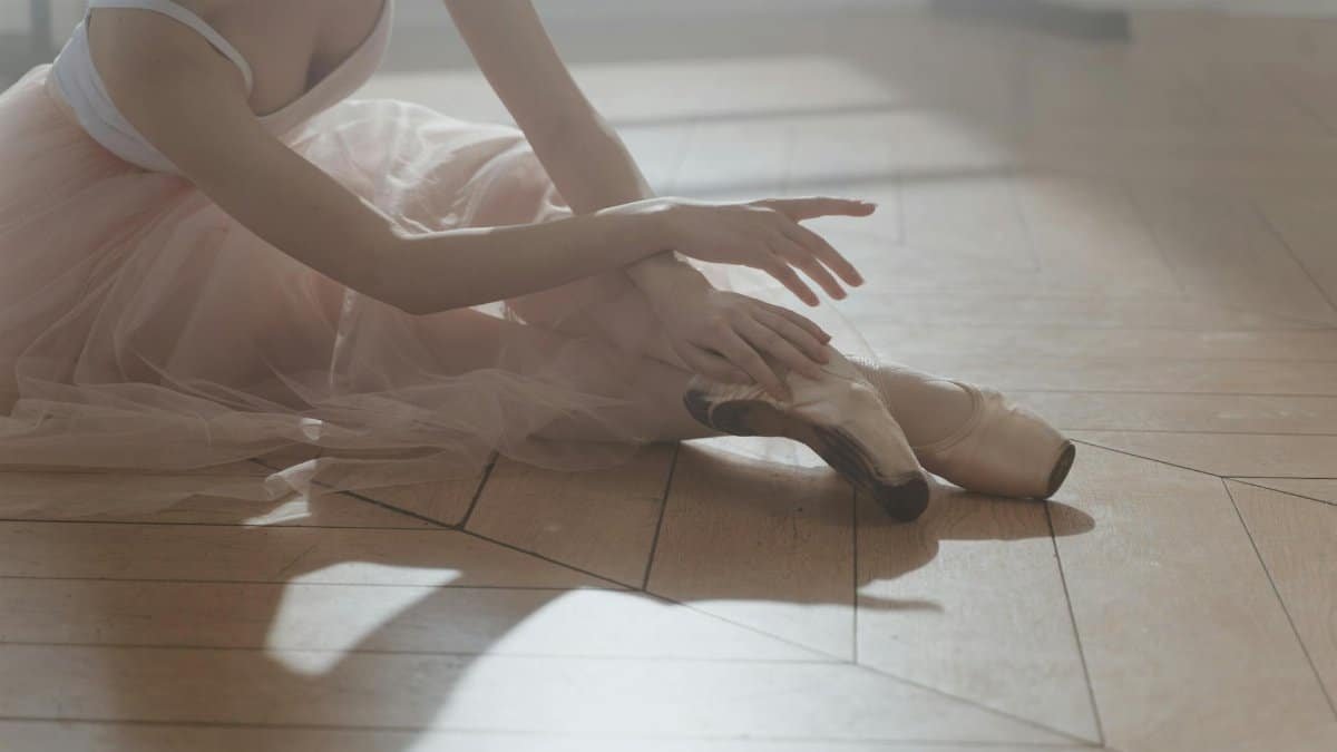 Delicate ballerina in pastel attire gracefully poised on a wooden floor.