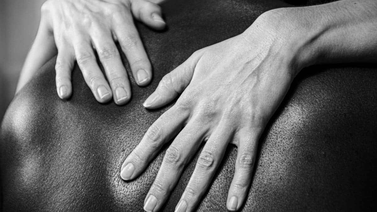 Artistic black and white photo of hands resting on a person's back, highlighting textures.
