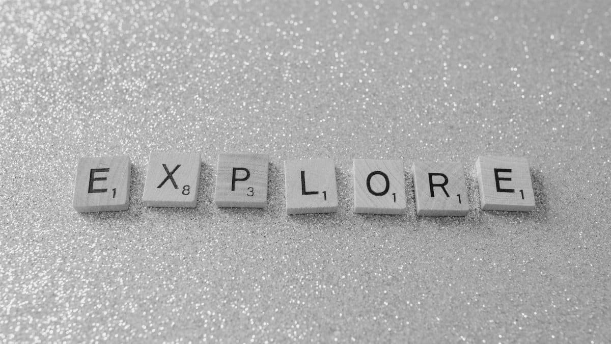 Monochrome Scrabble tiles spelling 'EXPLORE' on a glitter background.
