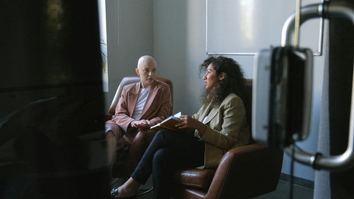Young female colleagues in trendy outfits sitting in armchairs and talking in meeting room