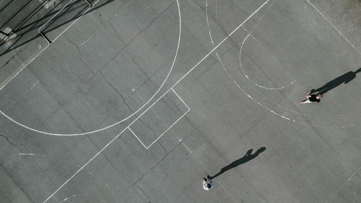 Aerial view of a basketball court with two players and long shadows cast in daylight.